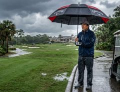 Golfer holding a large waterproof golf umbrella on a Florida golf course during a heavy afternoon rainstorm