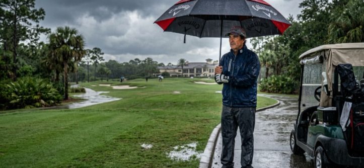Golfer holding a large waterproof golf umbrella on a Florida golf course during a heavy afternoon rainstorm