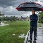 Golfer holding a large waterproof golf umbrella on a Florida golf course during a heavy afternoon rainstorm
