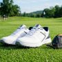 A pair of modern spiked golf shoes sitting on lush green golf course grass.