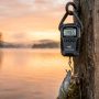 Digital portable fish scale hanging over serene lake at sunrise.