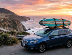 Surfboard securely mounted on a vehicle roof rack along a coastal California highway.