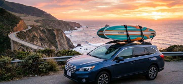 Surfboard securely mounted on a vehicle roof rack along a coastal California highway.