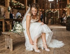 Texas bride sitting in a rustic venue smiling while trying on comfortable block heels.